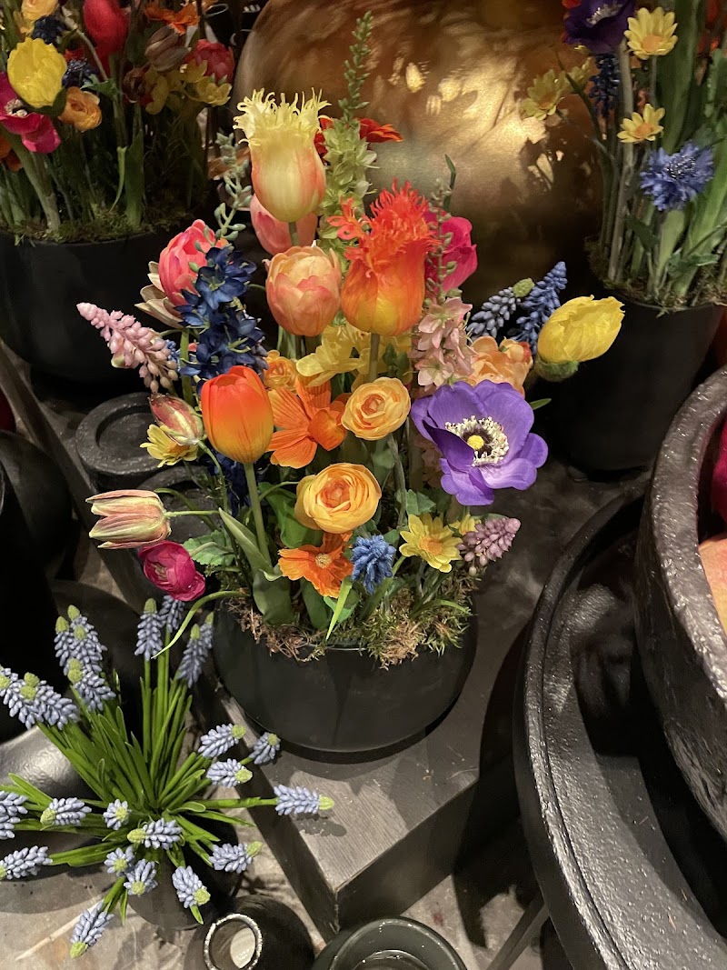 Voorjaarsarrangement van zijden bloemen: tulpen, ranonkels, anemoon en blauwe druifjes in een zwarte pot.